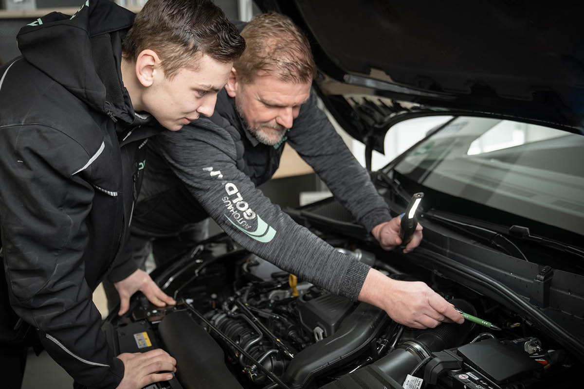 Lächelnder KFZ-Mechaniker steht unter einem Wagen, der auf einer Hebebühne steht